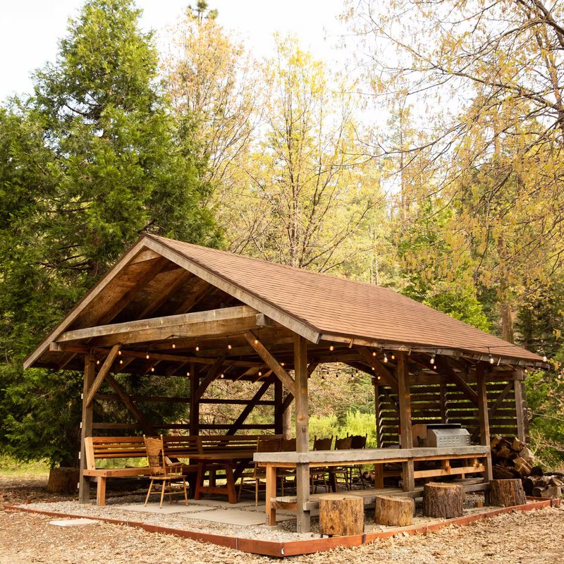 Timber-frame gazebo with BBQ, picnic table, string lights, and the firewood stack